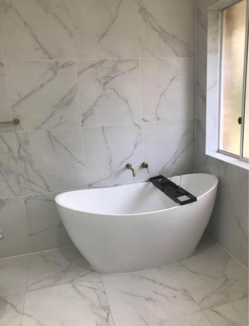 Completed marble bathroom renovation with freestanding bath and gold tapware
