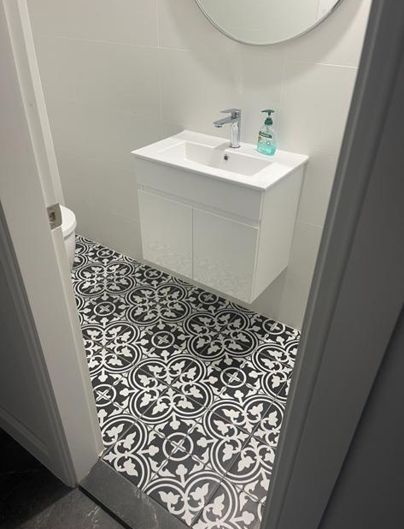 Powder room renovation with a white wall-hung vanity, round mirror and patterned floor tile