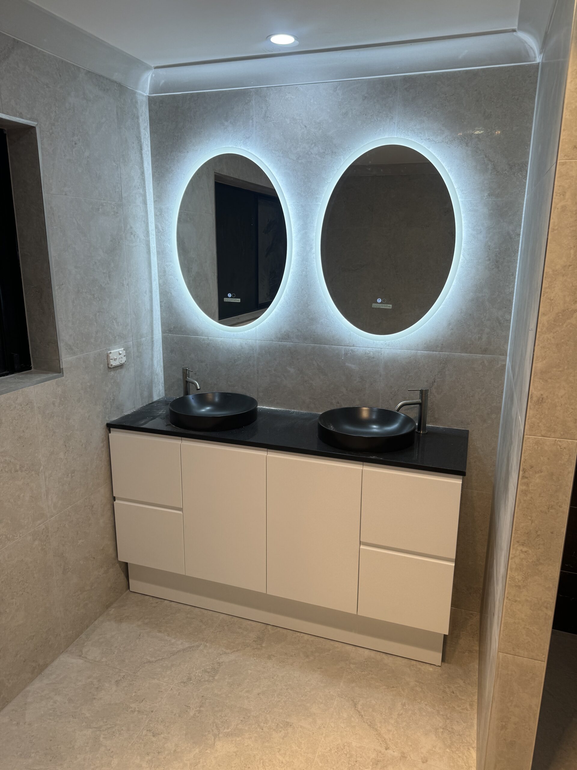 Bathroom renovation with twin backlit oval mirrors and black vessel basins